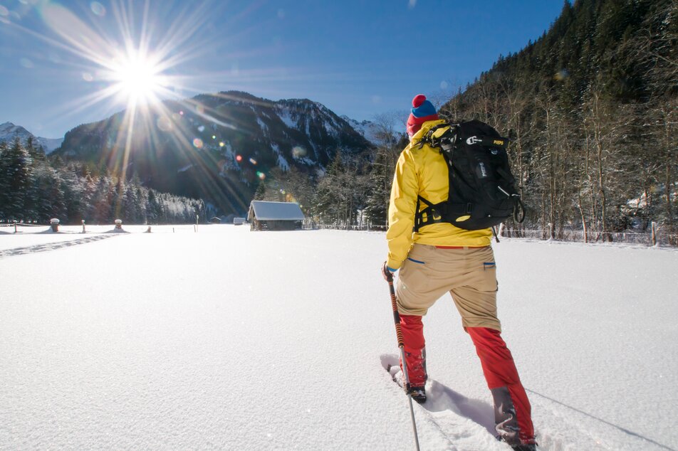 Ein Mann wandert mit den Schneeschuhen über eine große Wiese der Sonne entgegen | © Gerhard Pilz